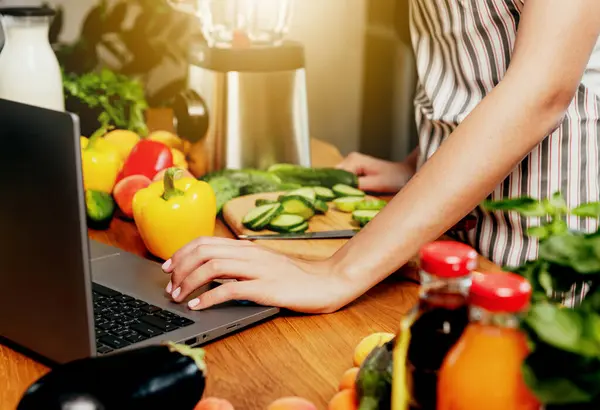 Young woman using laptop computer, girl hand clicking, touching pc. Person looking for recipe or watching tutorial. Fresh food on table at kitchen. Cooking healthy weight loss menu. Mobile diet app