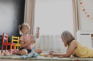 Çocuklar renkli oyuncaklarla oynuyorlar. Çocuklar evde, yatak odasında, anaokulunda, halının üzerinde oturuyorlar. Çocuk için eğitici çevre dostu bir oyun. Sevimli küçük kızlar birlikte kule inşa ediyorlar.