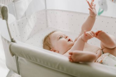 Cute little baby girl lying in the bed crib and playing with hanging mobile toy. Newborn care. Healthy childhood. Smiling infant, child or kid. High quality photo