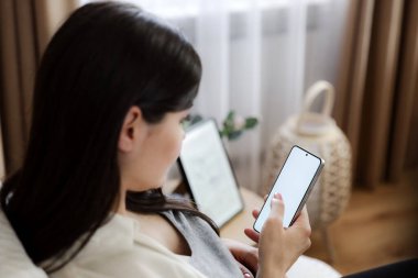 Bebek göbekli hamile bir kadın cep telefonunu beyaz ekranlı kullanıyor, online mağazayı arıyor, internet uygulamasını tarıyor. Yakın çekim, kopyalama alanı. Yemek sipariş etmek, sohbet etmek, otel rezervasyonu, uçak bileti.