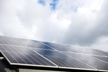 Bulutlardaki güneş paneli hücrelerinin hava görüntüsü, mavi gökyüzü arkaplanı. Doğa kavramında temiz alternatif enerji gücü, sürdürülebilir kaynaklar. Metal çatıda güneş paneli fotovoltaik santral sistemi olan ev