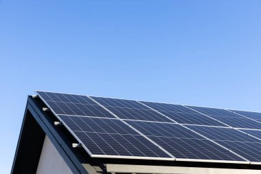 Evdeki metal kaplama çatı katında güneş panelleri olan tek başına fotovoltaik fabrika sistemi olan modern bir ev. Açık mavi gökyüzü arkaplanı. Temiz alternatif enerji kavramı. Profesyonel kurulum, yeşile dön