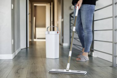 Modern ev ortamında yerleri paspaslayan, parlak ahşap silen bir kadın. Ev hanımı paspas ve kova kullanır. Oda servisi, ev işi konsepti. Uzayı kopyala Temizlik, temizlik, temizlik, temizlik, bakım.