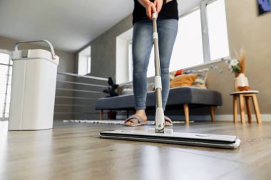 Modern ev ortamında yerleri paspaslayan, parlak ahşap silen bir kadın. Ev hanımı oturma odasında paspas, plastik kova ve macun kullanıyor. Oda servisi, ev işi, ev işleri konsepti.