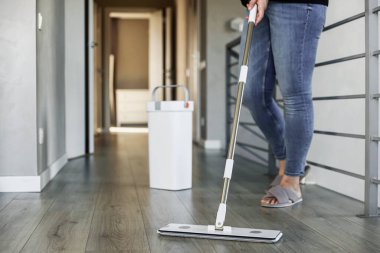 Modern ev ortamında yerleri paspaslayan, parlak ahşap silen bir kadın. Ev hanımı oturma odasında paspas, plastik kova ve macun kullanıyor. Oda servisi, ev işi, ev işleri konsepti.