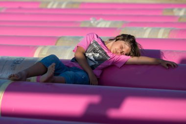 Pembe demiri boruların arasında pembe desenli bir tişört giymiş şirin beyaz çocuk. Moda tarzı fotoshoot