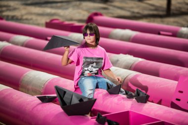 Pembe tişörtlü şirin bir çocuk siyah bulutlu, yağmurlu, mavi gökyüzüne karşı sanayi bölgesinde pembe borularla oynuyor. moda tarzı fotoshoot