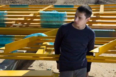 Çekici ve şık sarı saçlı beyaz adam ciddi bir yüzle poz veriyor. Endüstriyel bir alanda sarı demir yapıların arka planında. moda eğilimleri