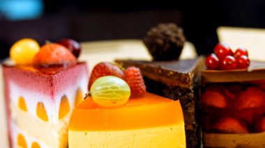 Açık bir kutuda birkaç dilim beyaz ve kırmızı çilekli ve kirazlı pasta ve çikolata. Makro ve kaydırma atışı. Arka planda bir retro atmosfer var..