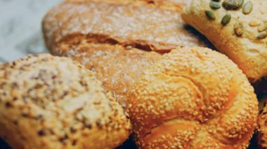 Ahşap masada farklı türde taze ekmek. Kahverengi arka planda münferit bir ekmek çeşidi. Kaydırıcı atışı.