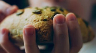 Kız çerçevesinde kabak çekirdeği olan bir somun taze kızarmış ekmek yayıyor. Arka planda romantik bir ortam var. Makro.