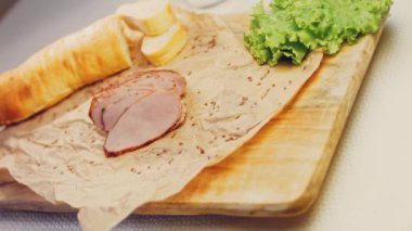 Fransız ekmeğiyle dilimlenmiş domuz filetosu. Sosis retro-stil yemek tepsisinde ve yemek kağıdında. Yavaş çekim kaydırağın üzerinde. Taze marul yaprakları da kullanıyoruz..