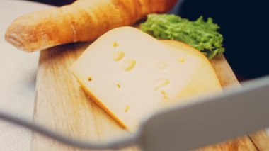 Retro-stil yemek tepsisinde delikleri olan peynir. Kaypak peynir sunum sürecini kaydetti. Arka planda Fransız ekmeği ve taze marul yaprakları var..