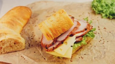 Fransız ekmeği, peynir, marul ve sosisli sandviç. Kaydırma atışı. Arka planda eski bir fırın tepsisi ve yemek kağıdı var..