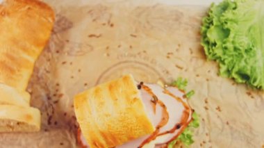 Fransız ekmeği, peynir, marul ve sosisli sandviç. Kaydırma atışı. Arka planda eski bir fırın tepsisi ve yemek kağıdı var..