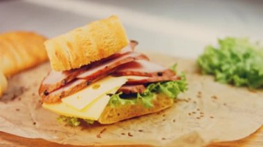 Fransız ekmeği, peynir, marul ve sosisli sandviç. Kaydırma atışı. Arka planda eski bir fırın tepsisi ve yemek kağıdı var..