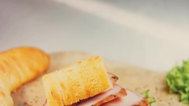 Fransız ekmeği, peynir, marul ve sosisli sandviç. Kaydırma atışı. Arka planda eski bir fırın tepsisi ve yemek kağıdı var..