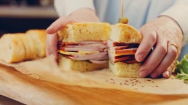 Şef iki dilim sandviçi Fransız ekmeği, peynir, marul ve sosisle açıyor. Kaydırma atışı. Arka planda eski bir fırın tepsisi ve yemek kağıdı var..