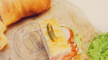 Fransız ekmeği, peynir, marul ve sosisli sandviç. Kaydırma atışı. Arka planda retro fırın tepsisi ve yemek kağıdı var. Üzerine küçük bir salatalık konmuş..