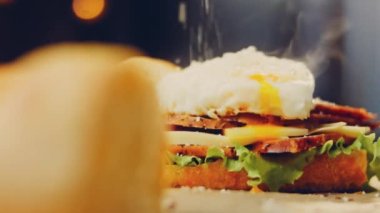 Şef kızarmış yumurtanın üzerine Fransız ekmeği, peynir, marul ve sosisle birlikte sanvich 'i buharla kaplayan bir kalp şeklinde parmesan serpiyor. Yumurta sarısı sandviçin üzerinden akıyor..