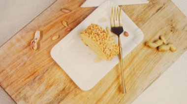 Kadın, altın çatallı fıstıkla sarılmış bir parça kek alıyor. Arka planda retro-stil yemek tepsisi üzerinde soyulmuş fıstık var. Makro ve sürgülü atış.