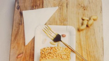 Kadın, altın çatallı fıstıkla sarılmış bir parça kek alıyor. Arka planda retro-stil yemek tepsisi üzerinde soyulmuş fıstık var. Makro ve sürgülü atış.