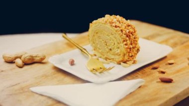 Kadın, altın çatallı fıstıkla sarılmış bir parça kek alıyor. Arka planda retro-stil yemek tepsisi üzerinde soyulmuş fıstık var. Makro ve sürgülü atış.