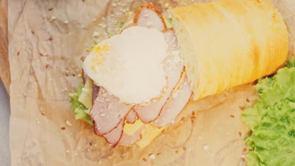 シェフは フランスのバゲット チーズ レタス ソーセージでサンドイッチの上を蒸気の心の形で揚げ卵の上にパルメザンチーズを振りかける 黄身がサンドイッチの上を流れる — ストック動画