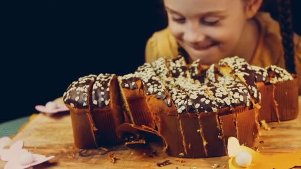 女の子はチョコレートケーキを見ると幸せといちゃつく 背景には 紙で作られたイースターのパージがあります マクロ撮影とスライダー撮影 — ストック動画
