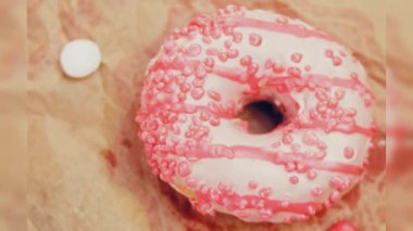 Pembe kremayla süslenmiş pembe çörekler. Çörekler şekerle süslenmiş bir kağıt parçasının üzerinde. Makro ve kaydırma atışı. Şekerler ağır çekimde hareket ediyor. Fırın ve yemek konsepti. Çeşitli renkli çörekler.