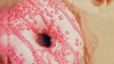 Pembe kremayla süslenmiş pembe çörekler. Çörekler şekerle süslenmiş bir kağıt parçasının üzerinde. Makro ve kaydırma atışı. Şekerler ağır çekimde hareket ediyor. Fırın ve yemek konsepti. Çeşitli renkli çörekler.