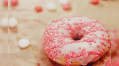 Pembe kremayla süslenmiş pembe çörekler. Çörekler şekerle süslenmiş bir kağıt parçasının üzerinde. Makro ve kaydırma atışı. Şekerler ağır çekimde hareket ediyor. Fırın ve yemek konsepti. Çeşitli renkli çörekler.