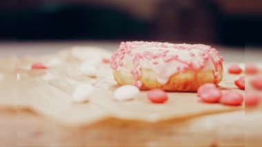 Pembe kremayla süslenmiş pembe çörekler. Çörekler şekerle süslenmiş bir kağıt parçasının üzerinde. Makro ve kaydırma atışı. Şekerler ağır çekimde hareket ediyor. Fırın ve yemek konsepti. Çeşitli renkli çörekler.