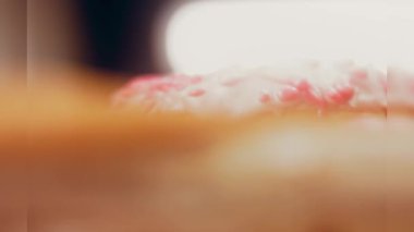 Pembe kremayla süslenmiş pembe çörekler. Çörekler şekerle süslenmiş bir kağıt parçasının üzerinde. Makro ve kaydırma atışı. Şekerler ağır çekimde hareket ediyor. Fırın ve yemek konsepti. Çeşitli renkli çörekler.