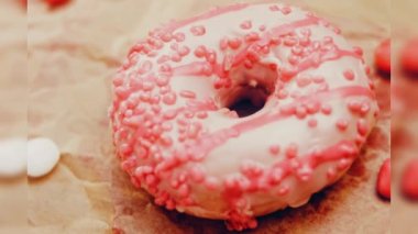 Pembe kremayla süslenmiş pembe çörekler. Çörekler şekerle süslenmiş bir kağıt parçasının üzerinde. Makro ve kaydırma atışı. Şekerler ağır çekimde hareket ediyor. Fırın ve yemek konsepti. Çeşitli renkli çörekler.