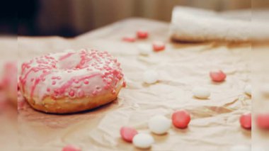 Pembe kremayla süslenmiş pembe çörekler. Çörekler şekerle süslenmiş bir kağıt parçasının üzerinde. Makro ve kaydırma atışı. Şekerler ağır çekimde hareket ediyor. Fırın ve yemek konsepti. Çeşitli renkli çörekler.