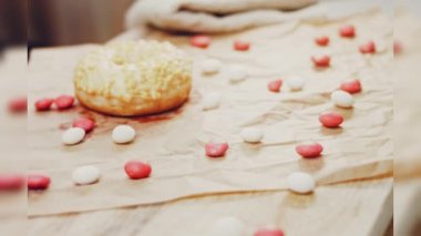 Sarı kremayla süslenmiş pembe çörekler. Çörekler şekerle süslenmiş bir kağıt parçasının üzerinde. Makro ve kaydırma atışı. Şekerler ağır çekimde hareket eder..