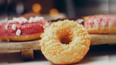 Çikolata, marşmelov ve retro pişirme tepsisindeki şekerli çörekler. Donutlar doğal çikolatayla süslenmiş bir kağıdın üzerinde. Makro ve kaydırma atışı. Çeşitli renkli çörekler. Çikolata, pembe, mavi çörekler