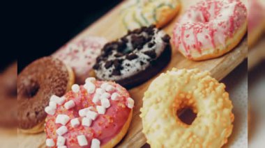 Çikolata, marşmelov ve retro pişirme tepsisindeki şekerli çörekler. Donutlar doğal çikolatayla süslenmiş bir kağıdın üzerinde. Makro ve kaydırma atışı. Çeşitli renkli çörekler. Çikolata, pembe, mavi çörekler