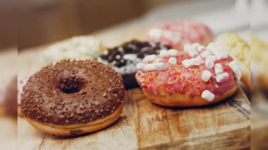 Çikolata, marşmelov ve retro pişirme tepsisindeki şekerli çörekler. Donutlar doğal çikolatayla süslenmiş bir kağıdın üzerinde. Makro ve kaydırma atışı. Çeşitli renkli çörekler. Çikolata, pembe, mavi çörekler