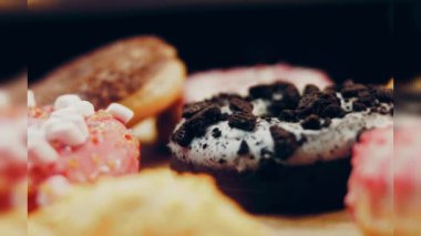 Çikolata, marşmelov ve retro pişirme tepsisindeki şekerli çörekler. Donutlar doğal çikolatayla süslenmiş bir kağıdın üzerinde. Makro ve kaydırma atışı. Çeşitli renkli çörekler. Çikolata, pembe, mavi çörekler