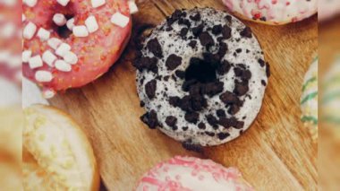 Çikolata, marşmelov ve retro pişirme tepsisindeki şekerli çörekler. Donutlar doğal çikolatayla süslenmiş bir kağıdın üzerinde. Makro ve kaydırma atışı. Çeşitli renkli çörekler. Çikolata, pembe, mavi çörekler