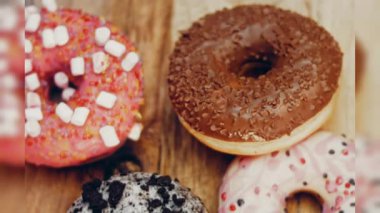 Çikolata, marşmelov ve retro pişirme tepsisindeki şekerli çörekler. Donutlar doğal çikolatayla süslenmiş bir kağıdın üzerinde. Makro ve kaydırma atışı. Çeşitli renkli çörekler. Çikolata, pembe, mavi çörekler