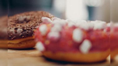 Çikolata, marşmelov ve retro pişirme tepsisindeki şekerli çörekler. Donutlar doğal çikolatayla süslenmiş bir kağıdın üzerinde. Makro ve kaydırma atışı. Çeşitli renkli çörekler. Çikolata, pembe, mavi çörekler