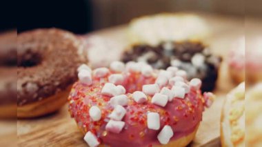 Çikolata, marşmelov ve retro pişirme tepsisindeki şekerli çörekler. Donutlar doğal çikolatayla süslenmiş bir kağıdın üzerinde. Makro ve kaydırma atışı. Çeşitli renkli çörekler. Çikolata, pembe, mavi çörekler