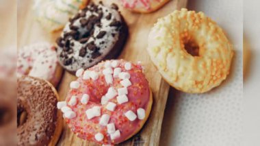 Çikolata, marşmelov ve retro pişirme tepsisindeki şekerli çörekler. Donutlar doğal çikolatayla süslenmiş bir kağıdın üzerinde. Makro ve kaydırma atışı. Çeşitli renkli çörekler. Çikolata, pembe, mavi çörekler