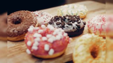 Çikolata, marşmelov ve retro pişirme tepsisindeki şekerli çörekler. Donutlar doğal çikolatayla süslenmiş bir kağıdın üzerinde. Makro ve kaydırma atışı. Çeşitli renkli çörekler. Çikolata, pembe, mavi çörekler