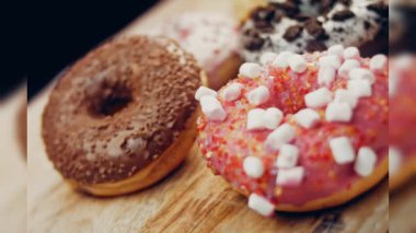 Çikolata, marşmelov ve retro pişirme tepsisindeki şekerli çörekler. Donutlar doğal çikolatayla süslenmiş bir kağıdın üzerinde. Makro ve kaydırma atışı. Çeşitli renkli çörekler. Çikolata, pembe, mavi çörekler