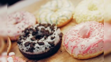 Çikolata, marşmelov ve retro pişirme tepsisindeki şekerli çörekler. Donutlar doğal çikolatayla süslenmiş bir kağıdın üzerinde. Makro ve kaydırma atışı. Çeşitli renkli çörekler. Çikolata, pembe, mavi çörekler