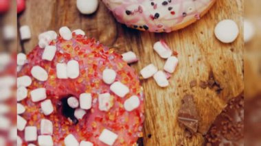 Çikolata, marşmelov ve retro pişirme tepsisindeki şekerli çörekler. Donutlar doğal çikolatayla süslenmiş bir kağıdın üzerinde. Makro ve kaydırma atışı. Çeşitli renkli çörekler. Çikolata, pembe, mavi çörekler